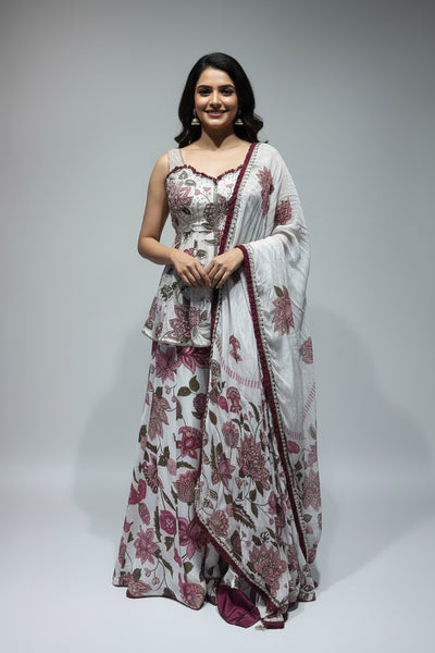 A white traditional outfit displayed on a mannequin, featuring a floral print in pink, red, and green, with a matching sheer dupatta draped over the shoulder.